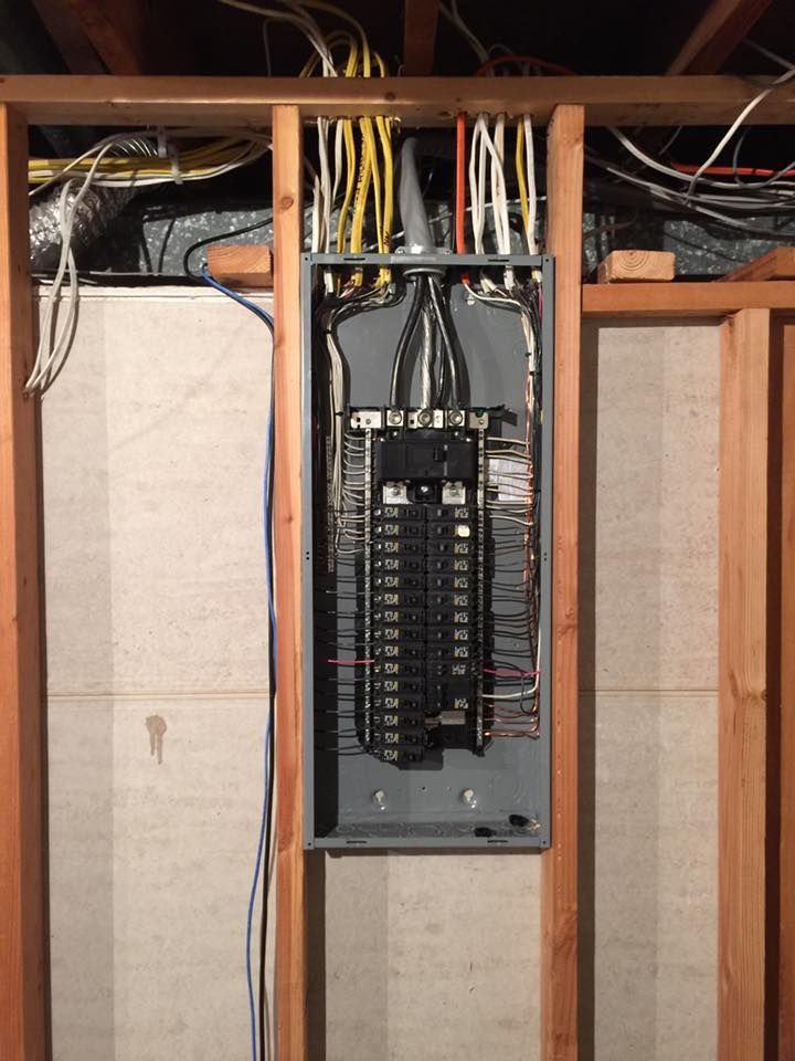 Electrical panel with numerous wires inside a wooden framed wall.