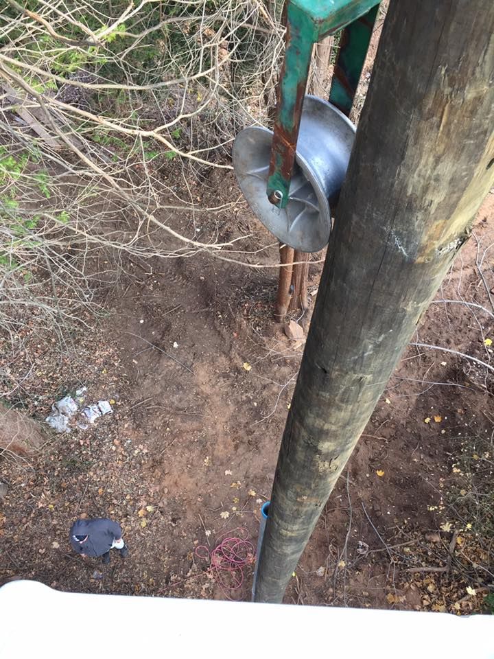 Overhead view of utility pole with pulley, likely for cables. Earth and trees in the background.