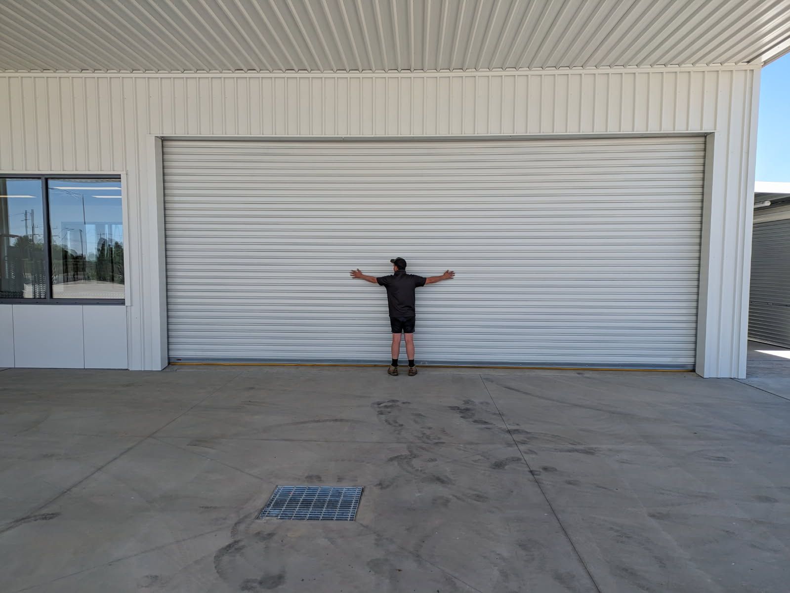 A man is standing in front of a garage door with his arms outstretched — Goldfields Garage Doors & Gates in Wendouree, VIC