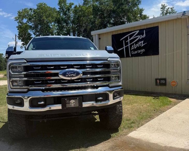 White pickup truck parked beside a beige building with a black sign in bright daylight