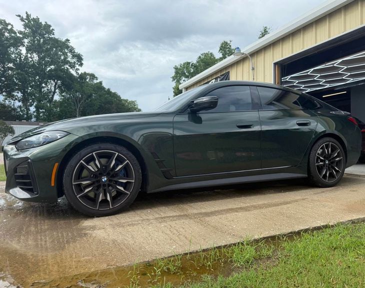 Dark green sports coupe parked on a driveway beside a garage under cloudy skies