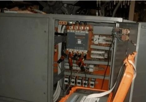 Quadro elettrico aperto con cablaggio, interruttori e cavi arancioni all'interno di un armadio.