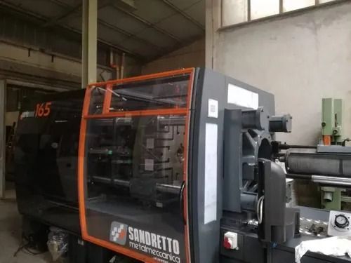 Macchinario industriale arancione e nero in un'officina, con porte di sicurezza trasparenti e rulli annessi
