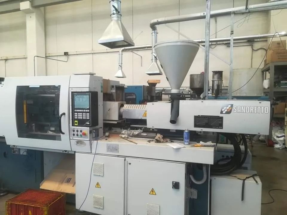 Pressa a iniezione industriale bianca in un'officina di fabbrica con pannello di controllo e tramoggia.