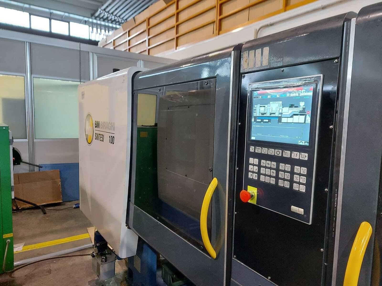 Macchinario industriale con pannelli in bianco e nero, maniglie gialle e schermo di controllo in un'officina di fabbrica.
