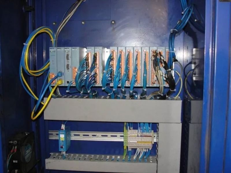 Armadio di controllo industriale blu con file di cablaggi, moduli di circuiti e cavi giallo-blu al suo interno.