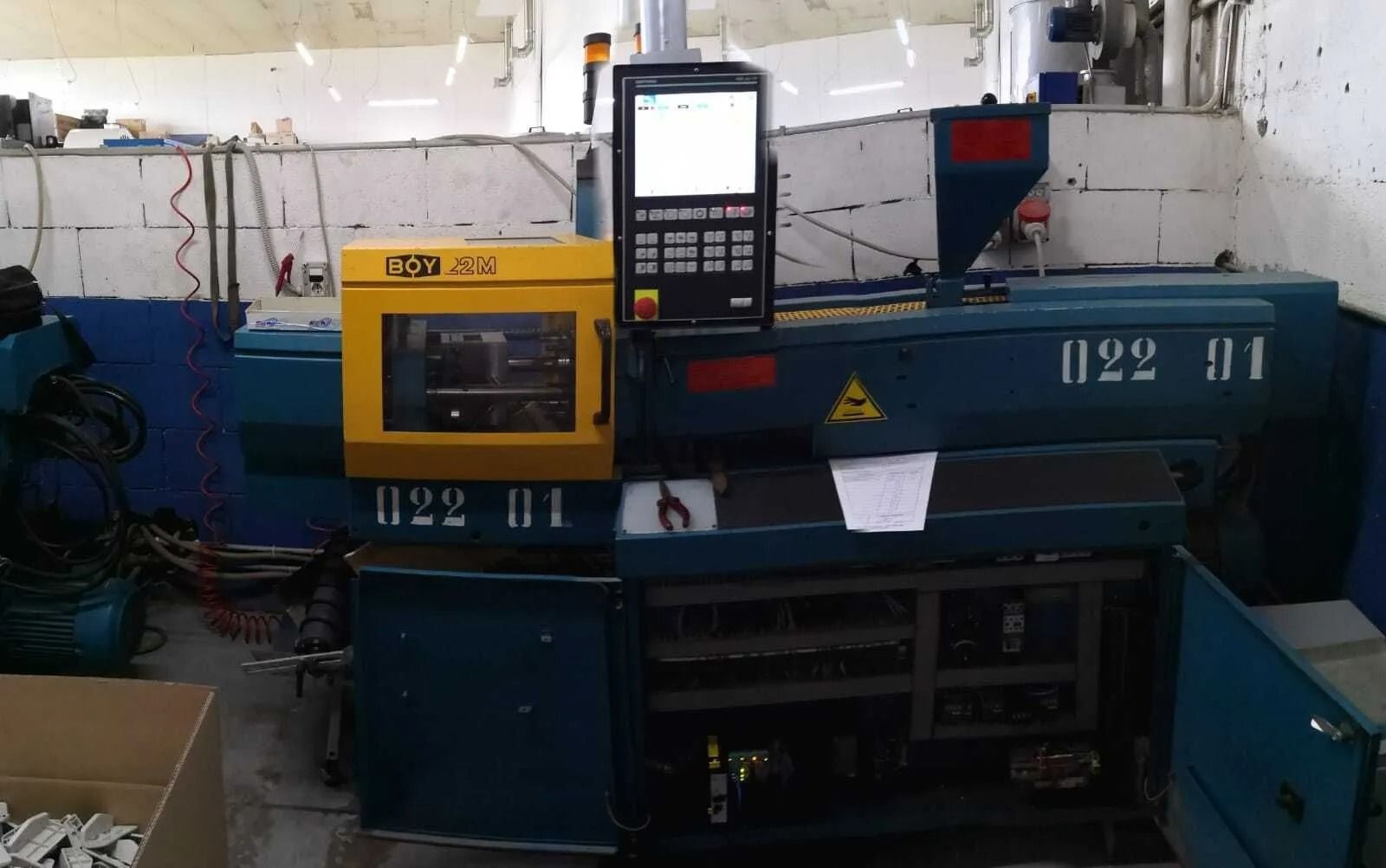 Macchinario industriale blu con pannello di controllo in un'officina, con cavi e utensili intorno.