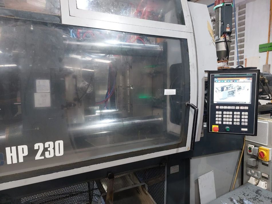 Pannello di controllo di una macchina industriale accanto a una grande macchina HP 230 grigia in un ambiente di fabbrica.