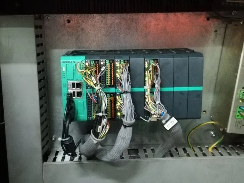 Armadio di controllo industriale con moduli PLC, cablaggio e morsetti montati all'interno di un contenitore metallico.