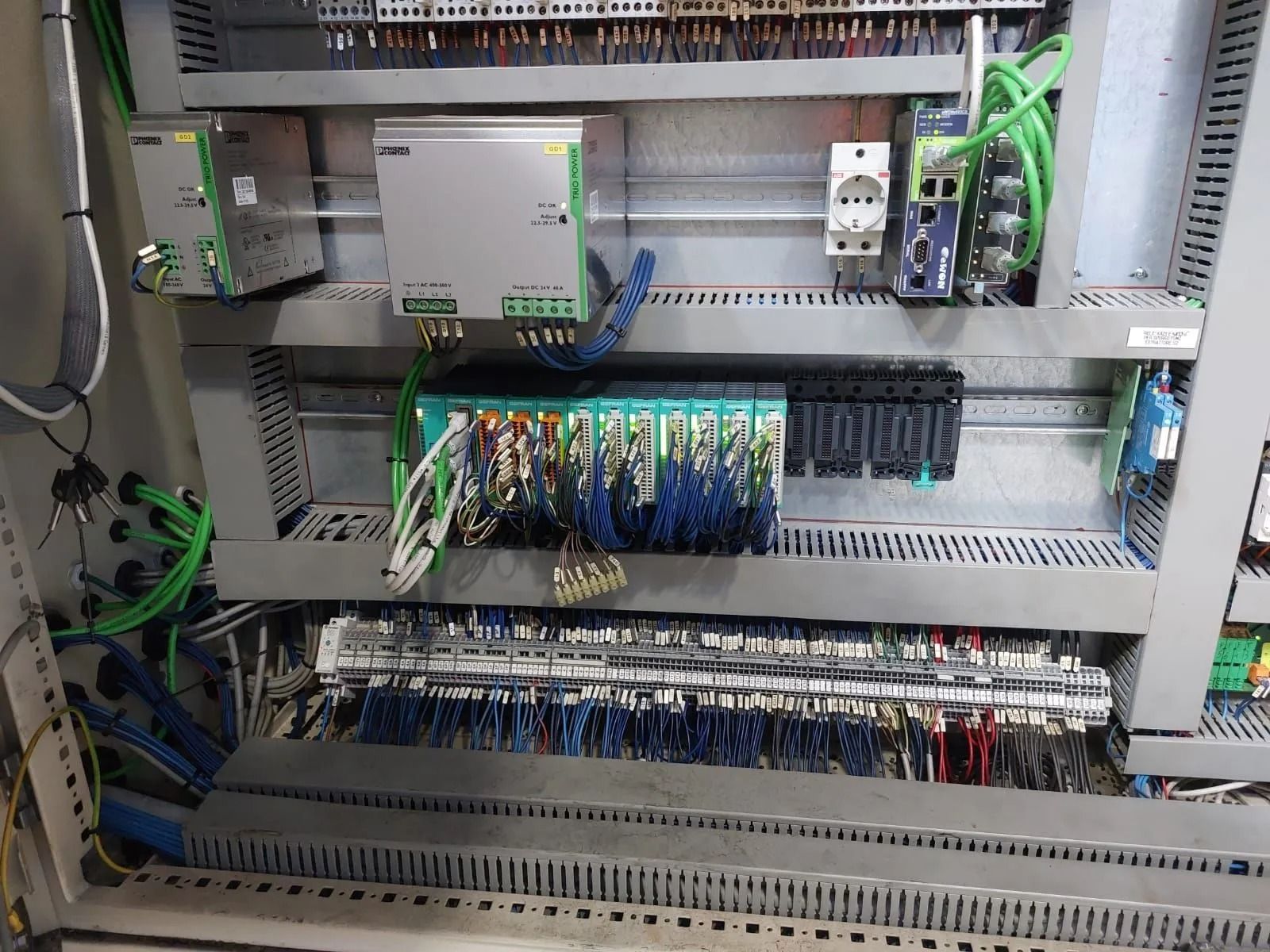 Quadro elettrico di controllo con file di relè, cablaggi e morsettiere all'interno di un armadio metallico.