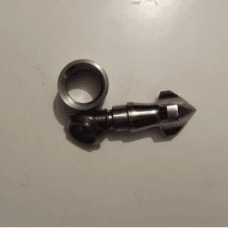 Piccolo componente metallico nero con un anello accanto, su una superficie grigio chiaro.