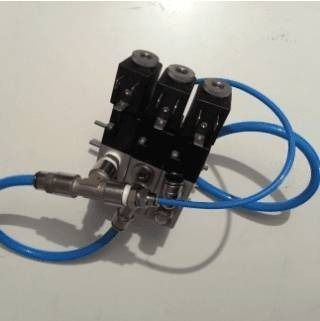 Primo piano di un piccolo gruppo di valvole pneumatiche con tubi blu su una superficie bianca.