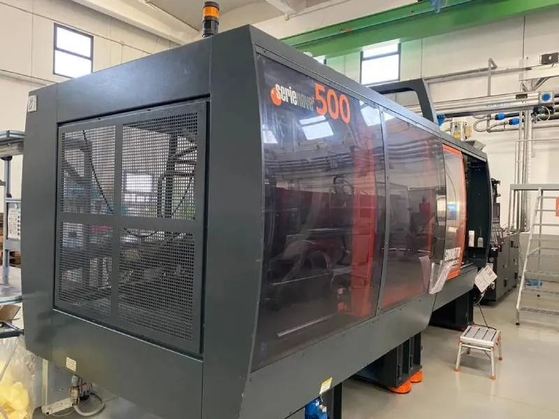 Grande macchinario industriale in una fabbrica, nero e rosso, con involucro di sicurezza e luce di segnalazione arancione.