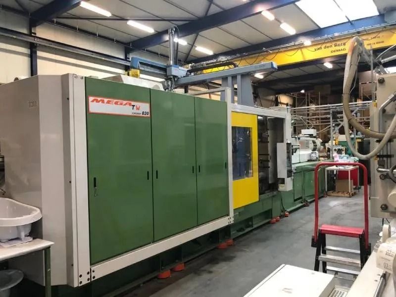 In una fabbrica, si trova una grande pressa industriale verde e bianca, con una sezione gialla e una gru a ponte.