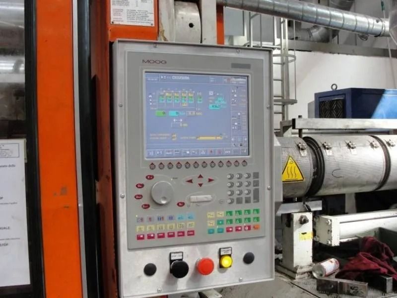 Pannello di controllo industriale con display, pulsanti e arresto di emergenza posizionato accanto a un macchinario in una fabbrica.