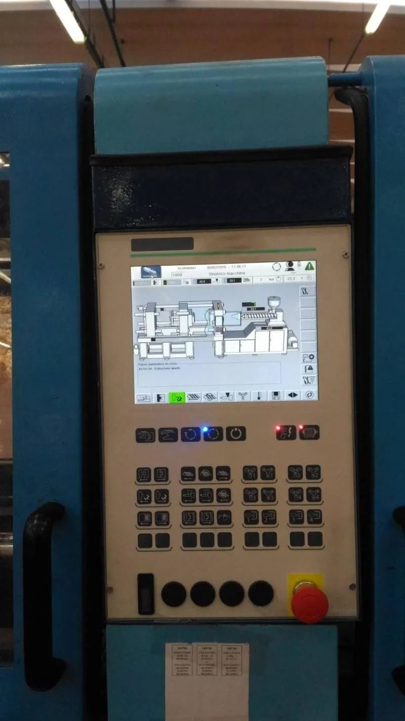 Pannello di controllo industriale con piccolo display, numerosi pulsanti e pulsante rosso di arresto di emergenza su una macchina blu