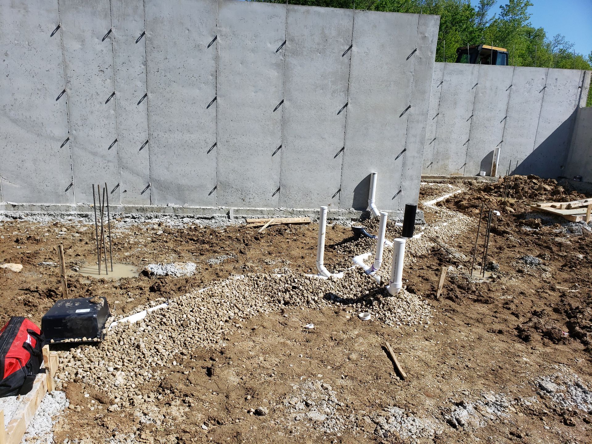 Construction site with gray retaining wall, exposed dirt, and white pipes near the ground