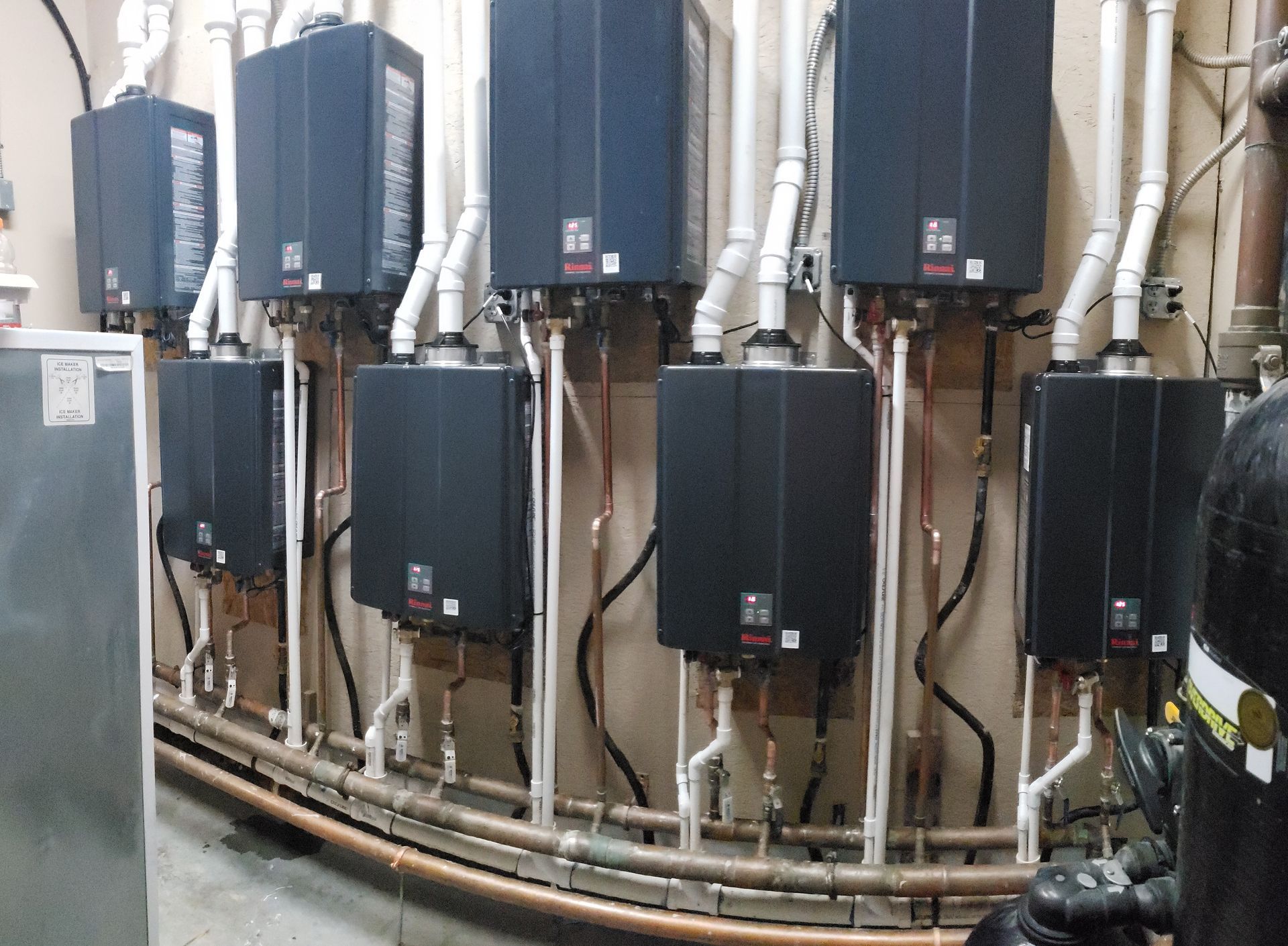 Row of gray wall-mounted electrical boxes with pipes and cables in a utility room