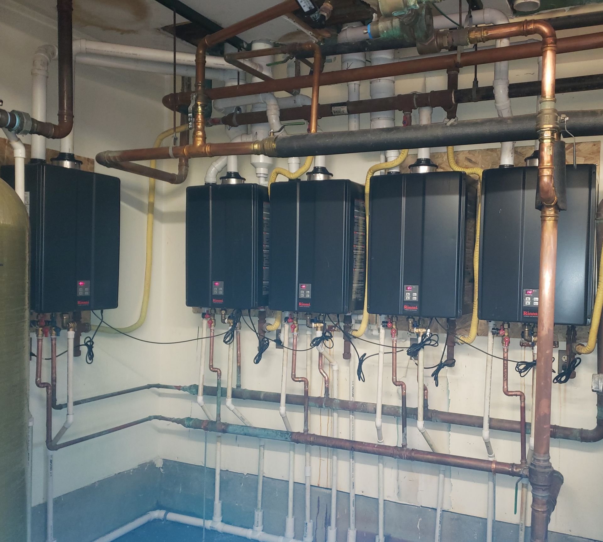 Row of wall-mounted black boiler units with copper piping in a utility room