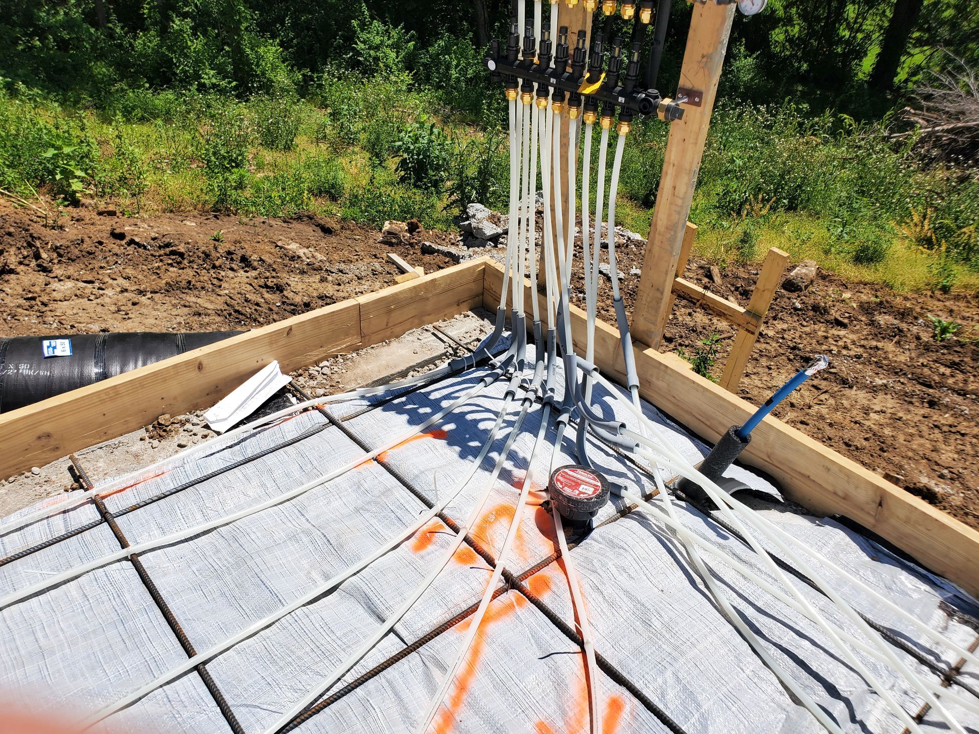 Concrete slab under construction with rebar and PVC pipes, surrounded by wooden forms and gravel