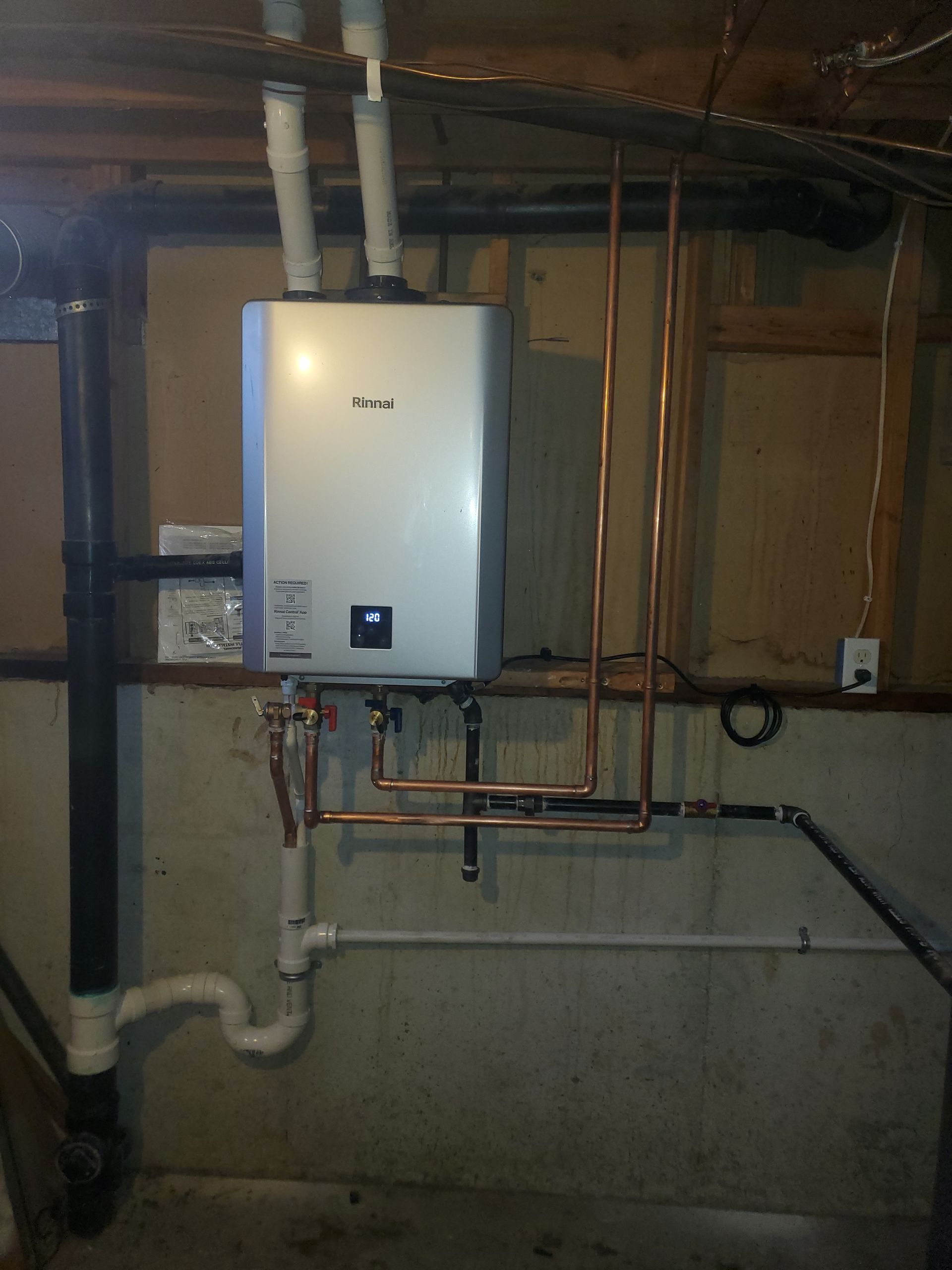 Basement wall with a white tankless water heater, copper pipes, and exposed utility lines.