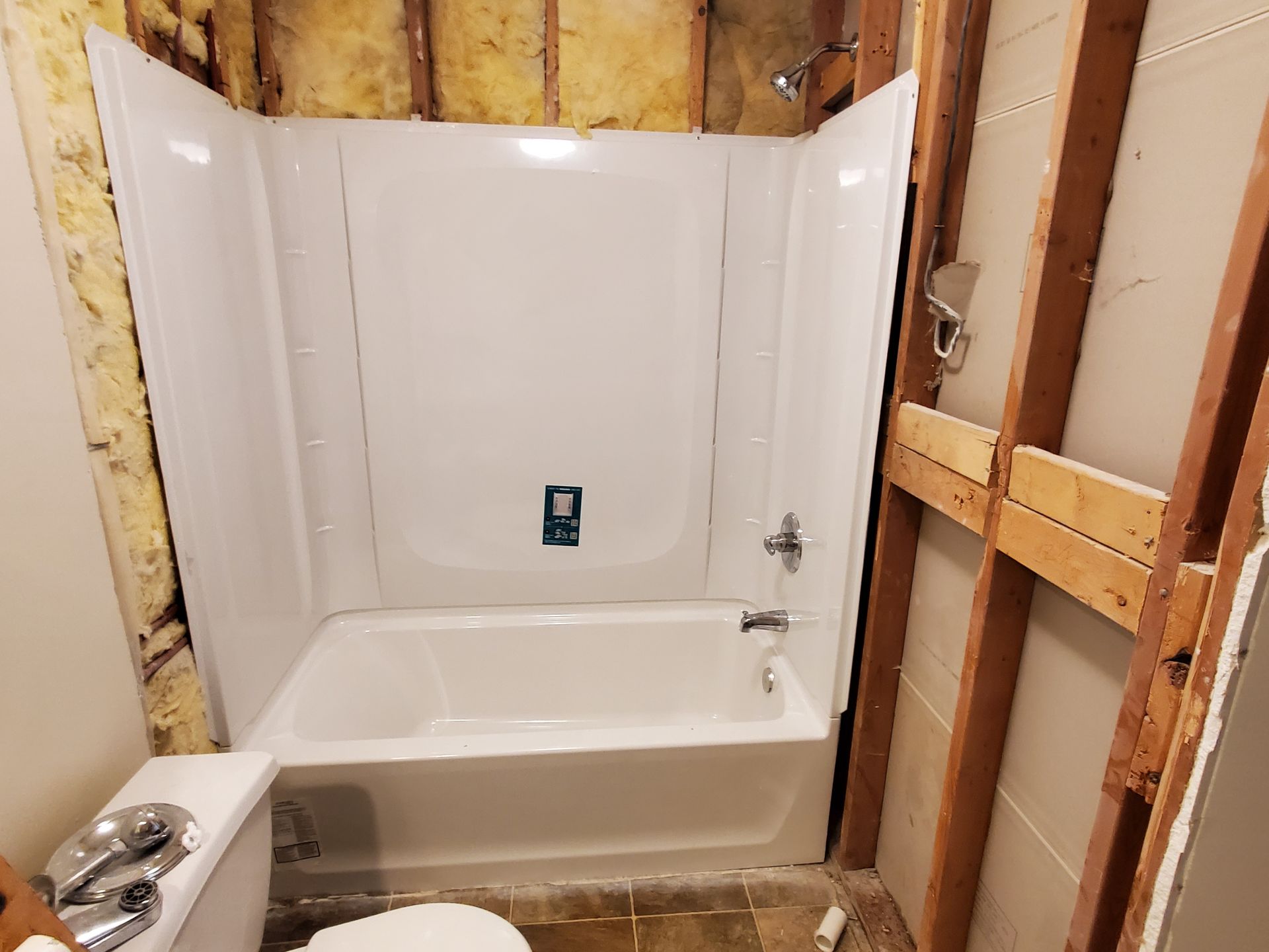 Bathtub shower alcove with white surround in a partially renovated bathroom