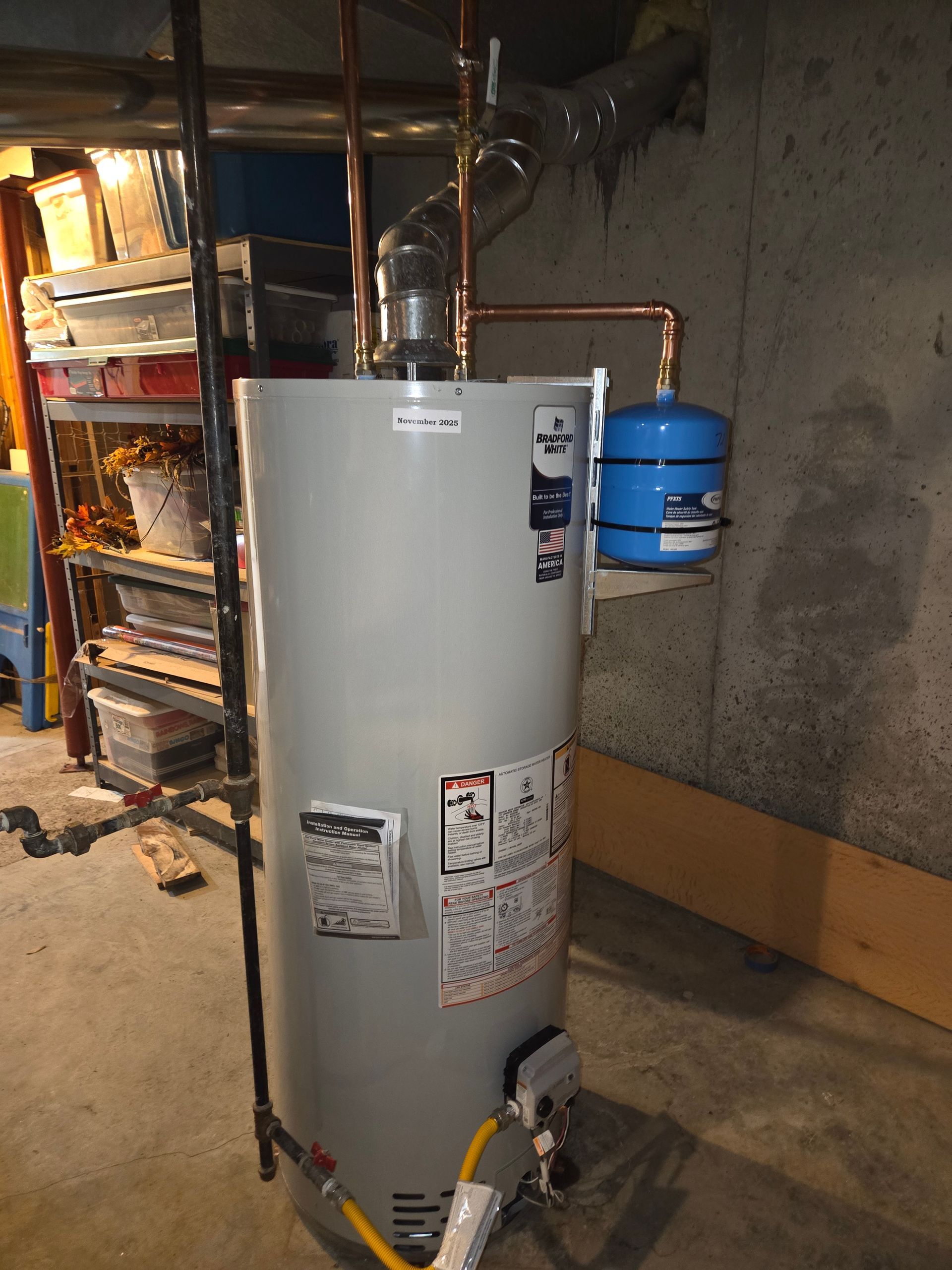 Tall gray water heater with blue expansion tank in a basement utility area.