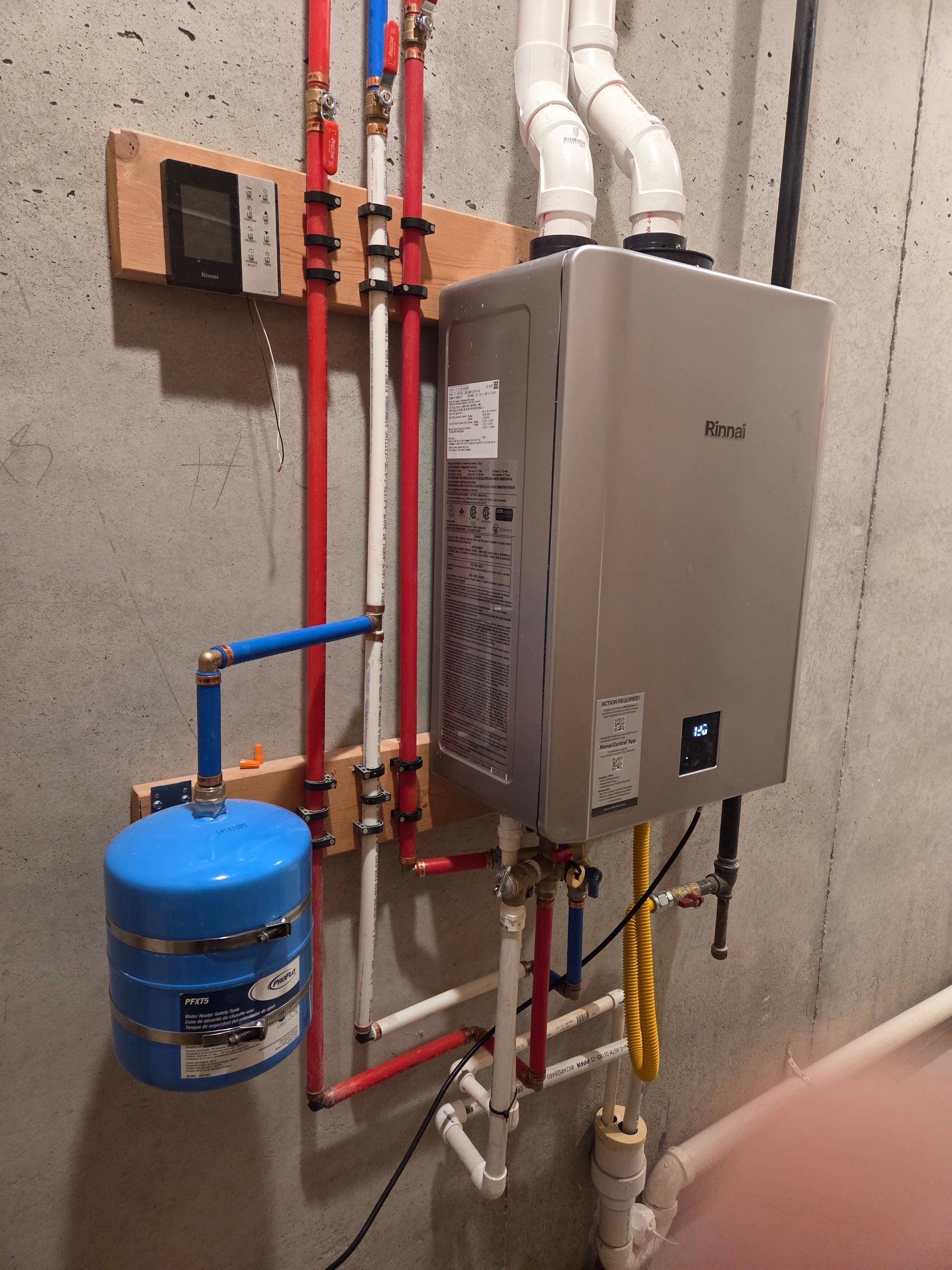 Wall-mounted tankless water heater with red and white pipes and a blue expansion tank in a utility room