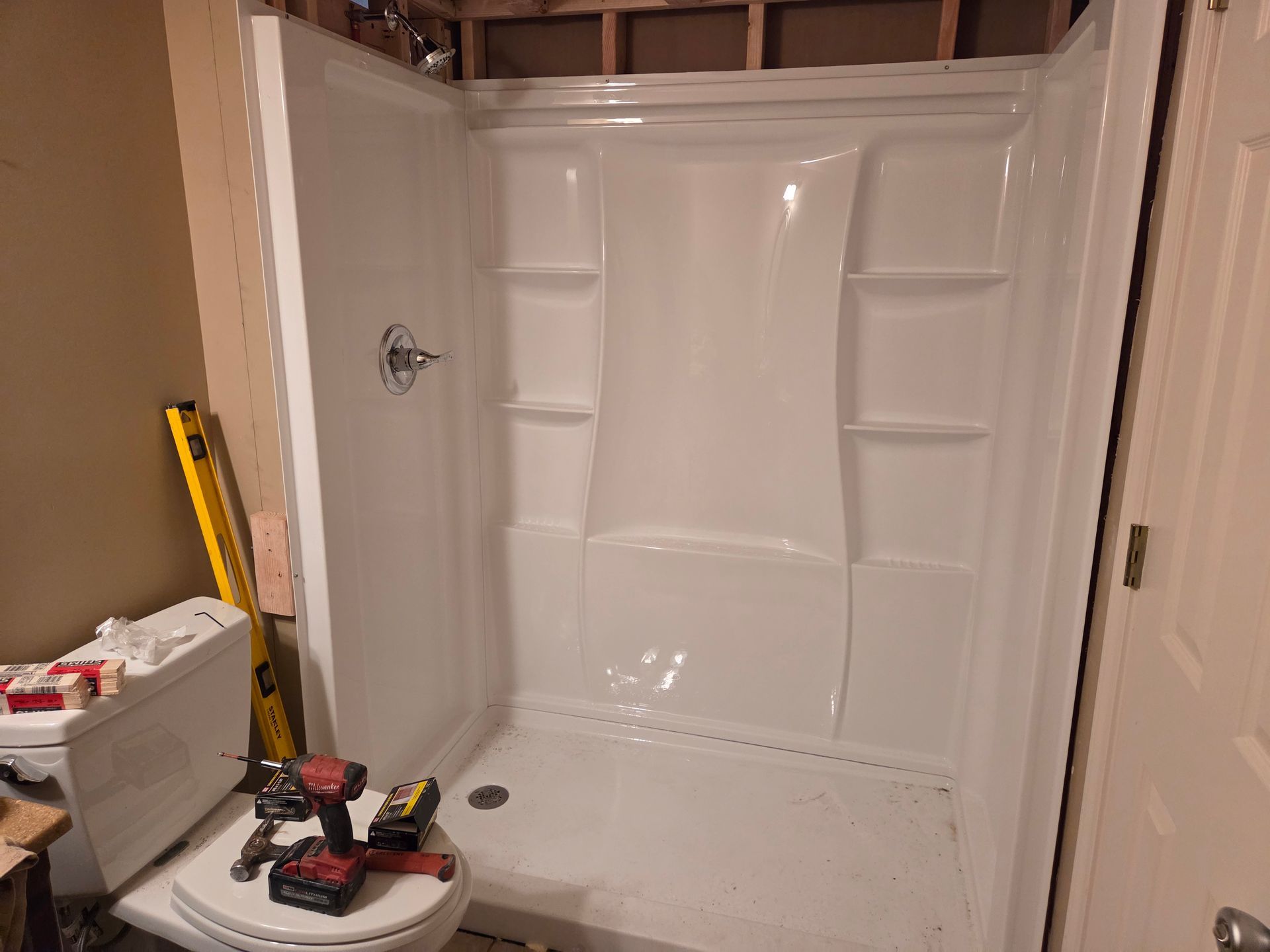 White bathtub being installed in a bathroom, with tools and a tape measure nearby.
