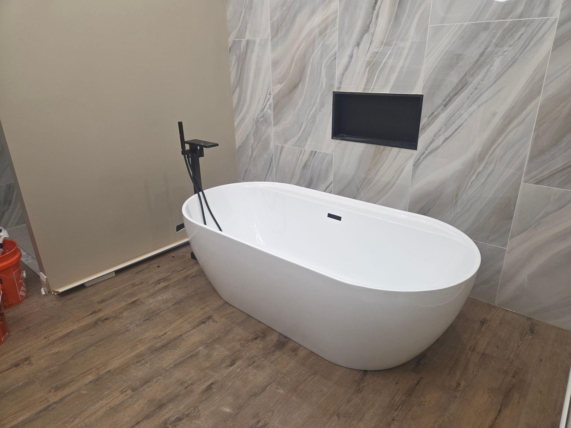 Modern bathroom with a white freestanding bathtub and black floor-mounted faucet against a tiled wall