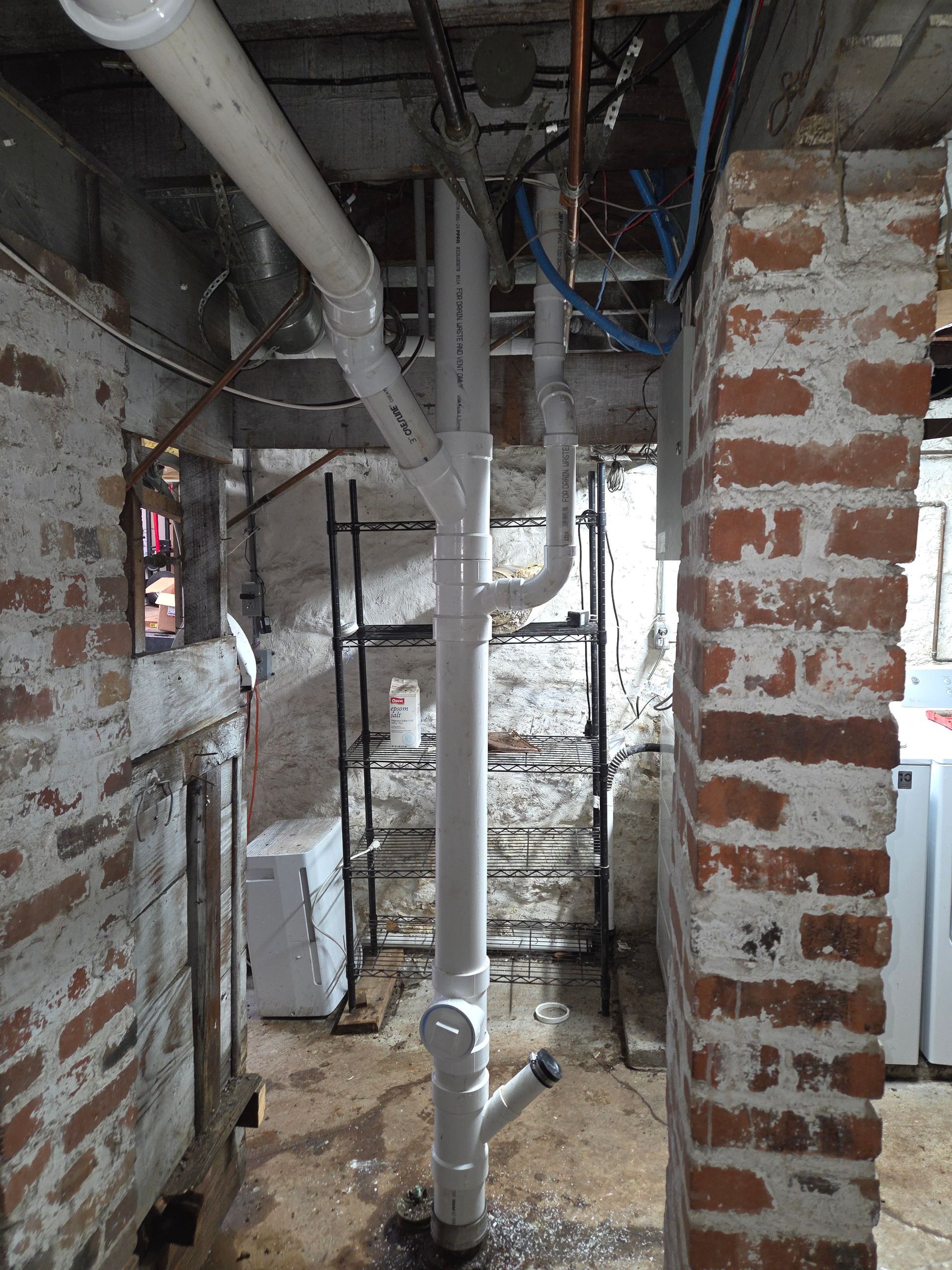 Unfinished indoor construction corridor with exposed pipes, brick walls, and debris on the floor