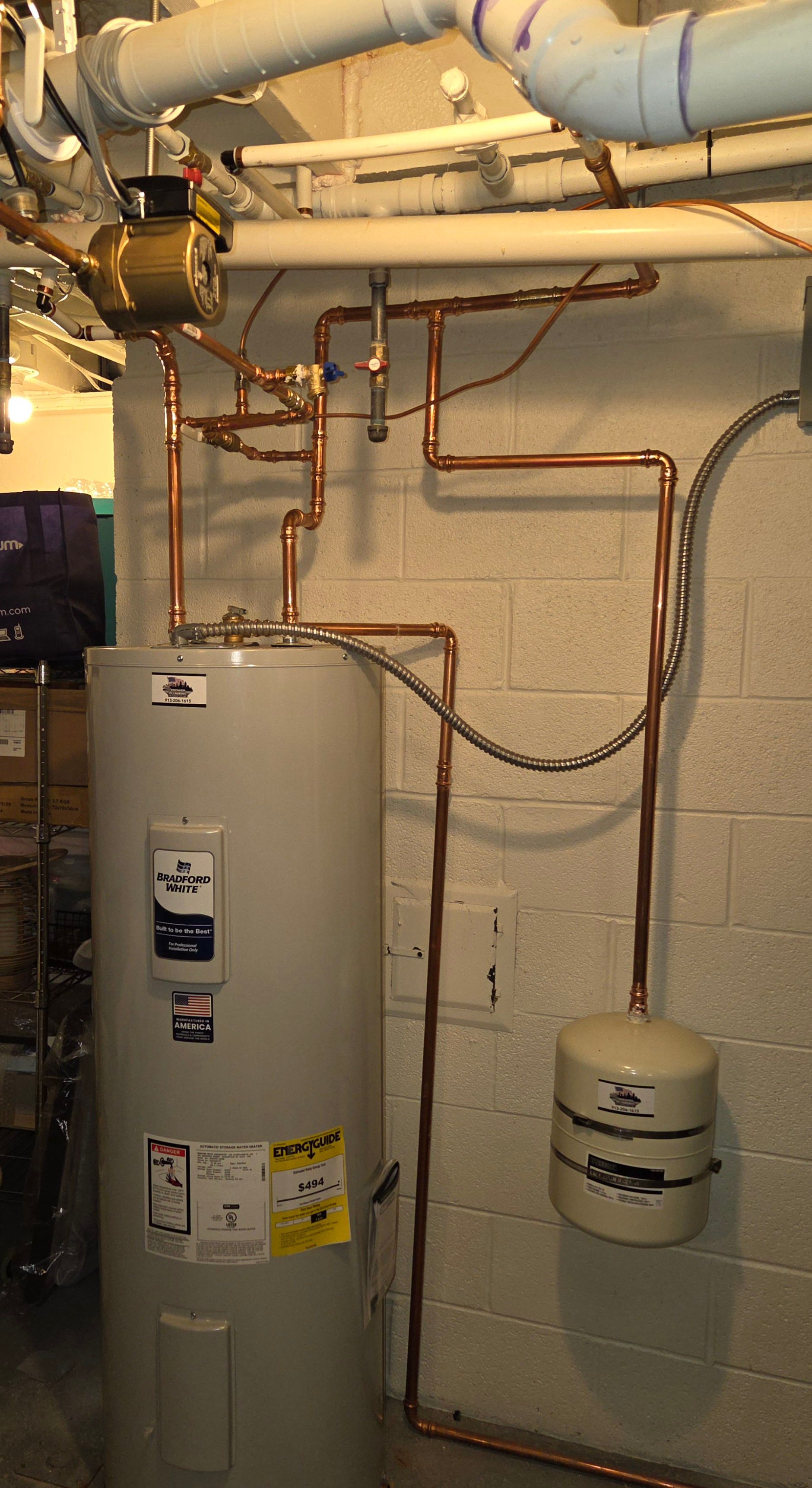 Water heater and copper plumbing pipes in a utility room, with a small expansion tank on the wall.