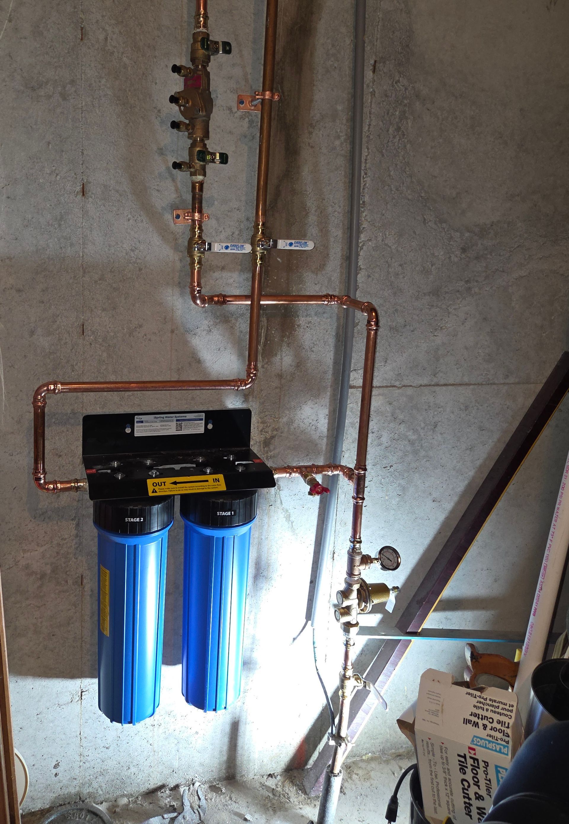 Blue water filter system with copper pipes installed against a concrete wall in a utility area