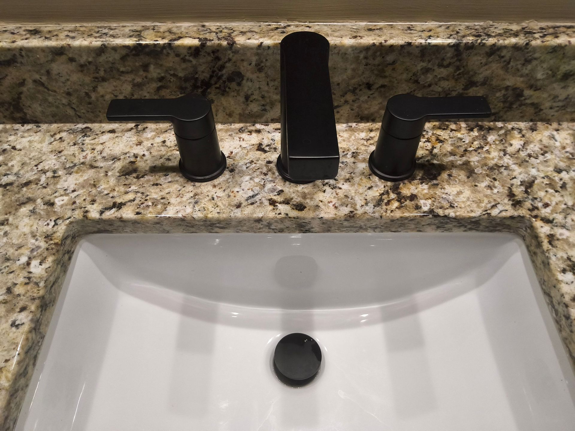 Black faucet over white bathroom sink with granite countertop and chrome handles
