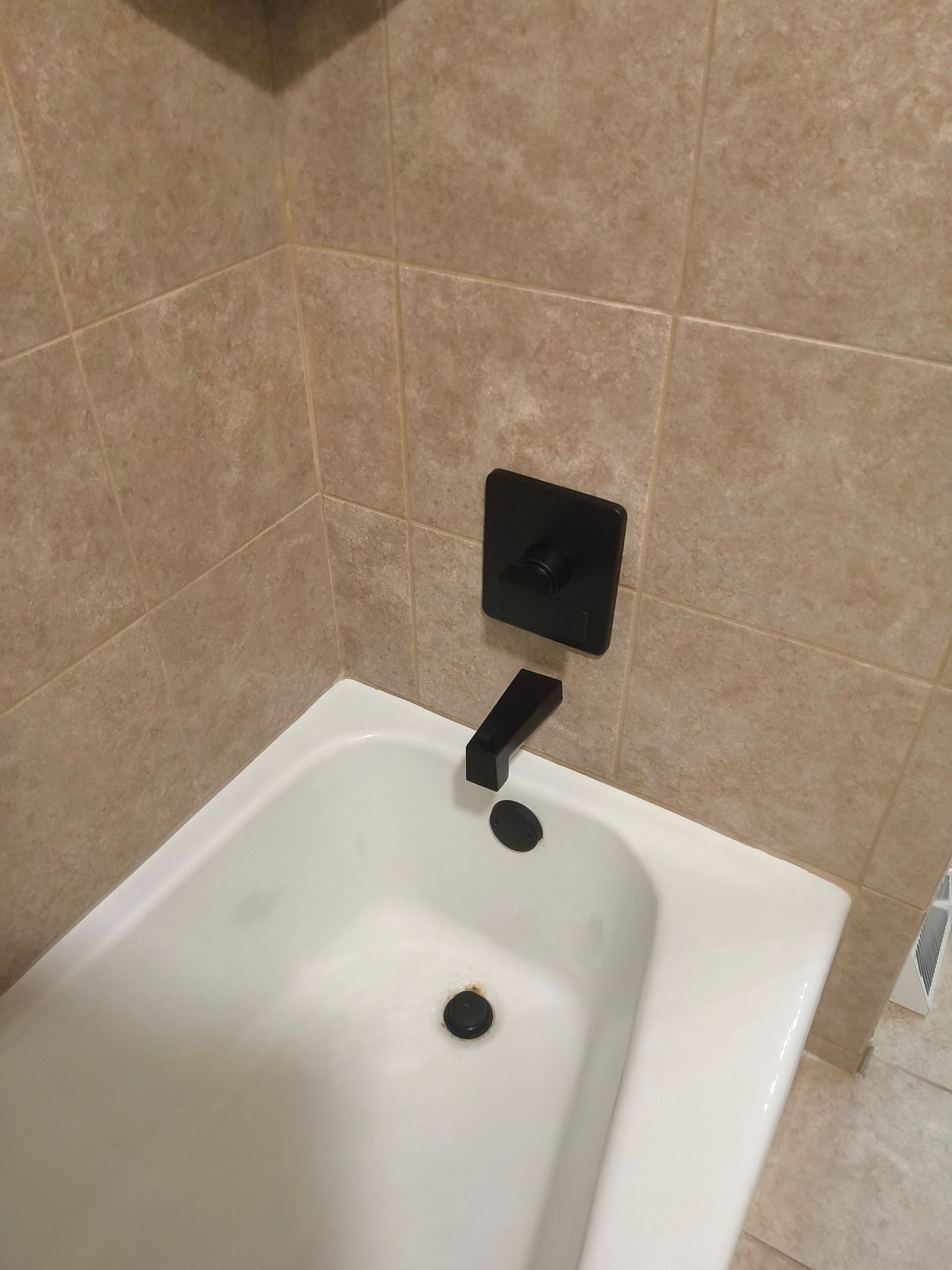 White bathtub with black faucet and drain against beige tiled bathroom wall