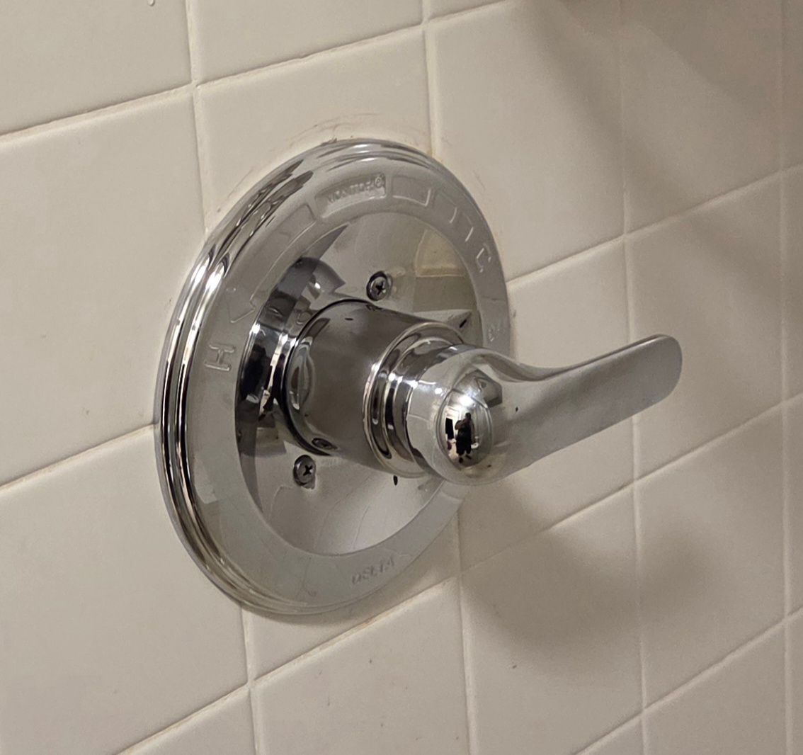 Chrome shower control handle on a tiled bathroom wall