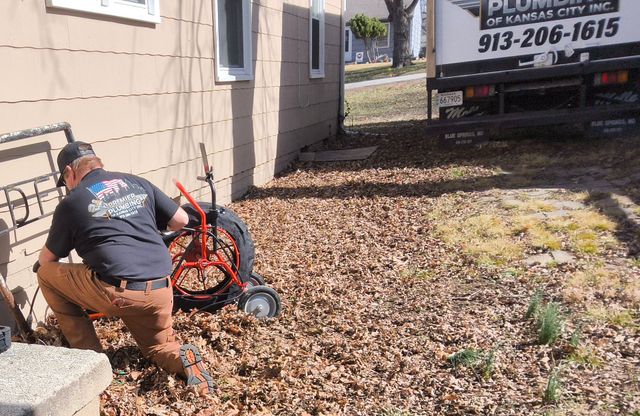 Worker using a wheelbarrow beside a house in a leaf-covered yard