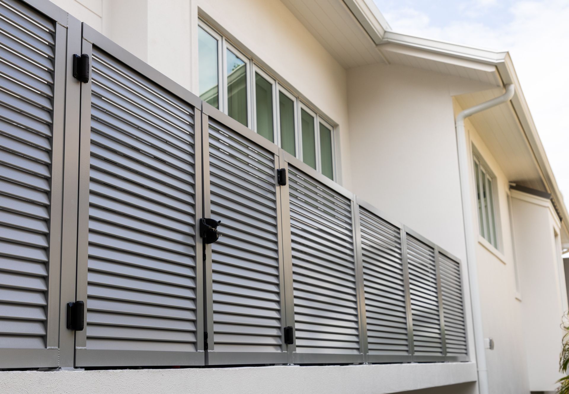 Row of gray louvered metal security gates on a white house exterior