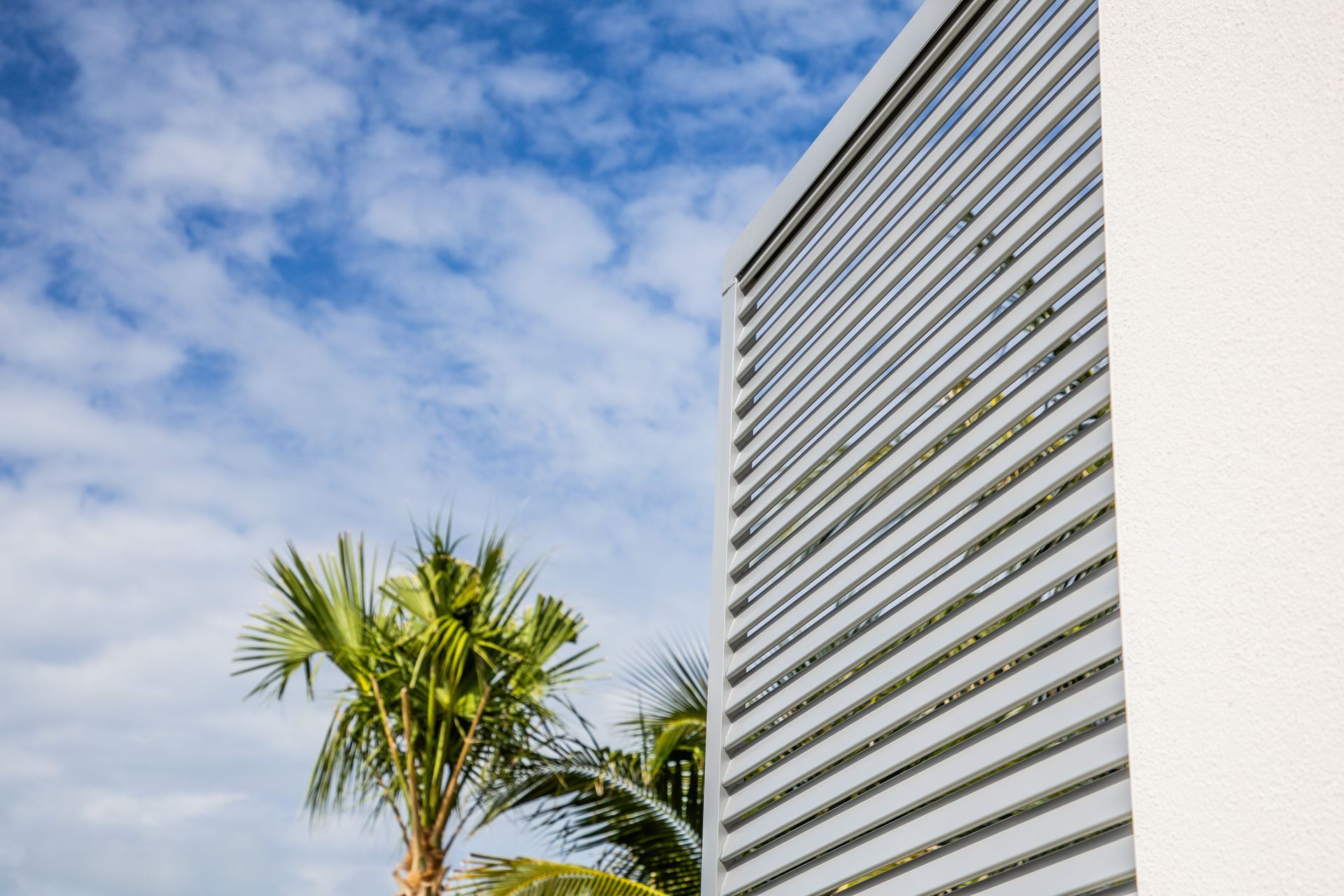 Tall white striped building beside palm trees under a blue, cloudy sky
