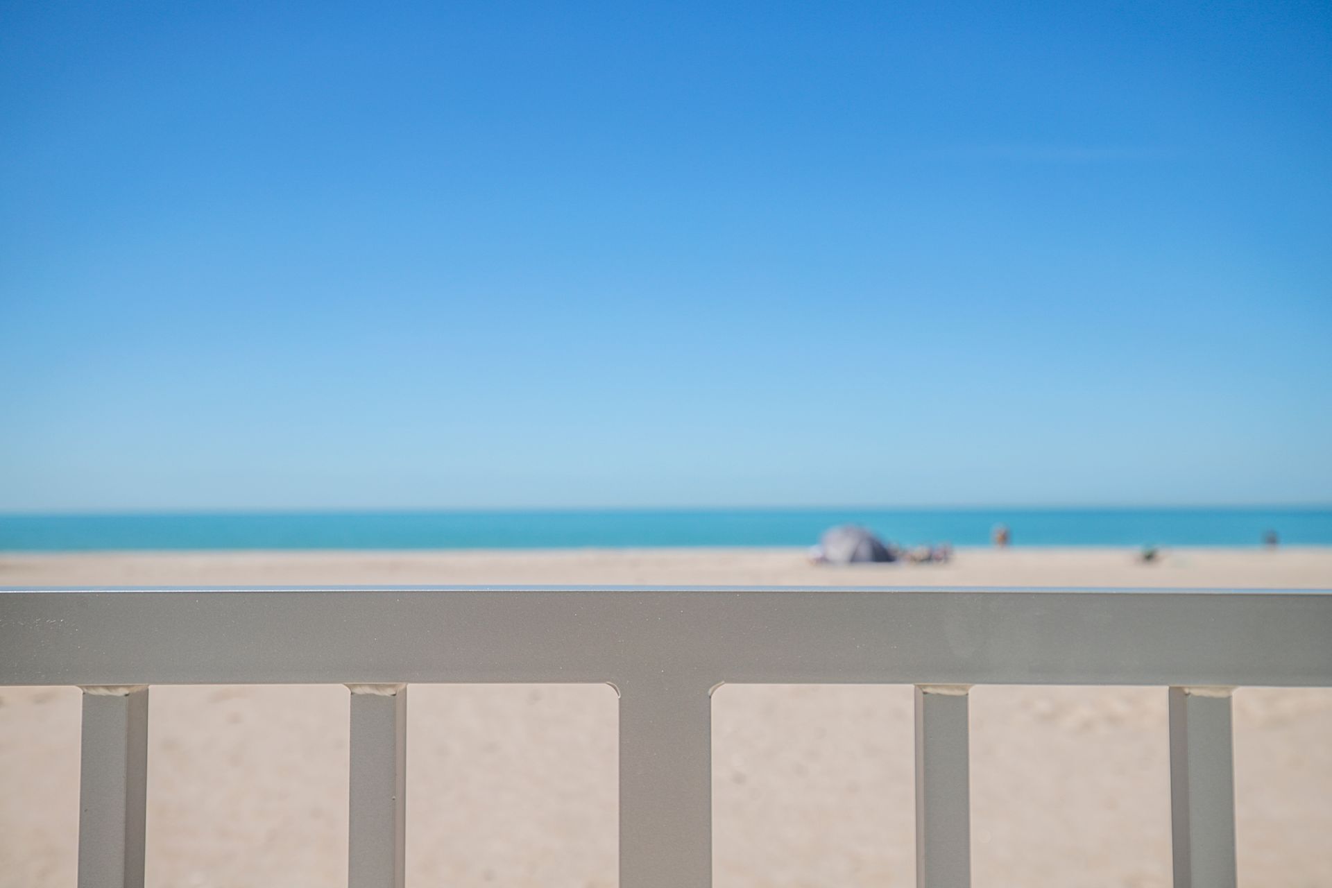 Bright beach scene with blue sky, turquoise sea, and white railing in the foreground