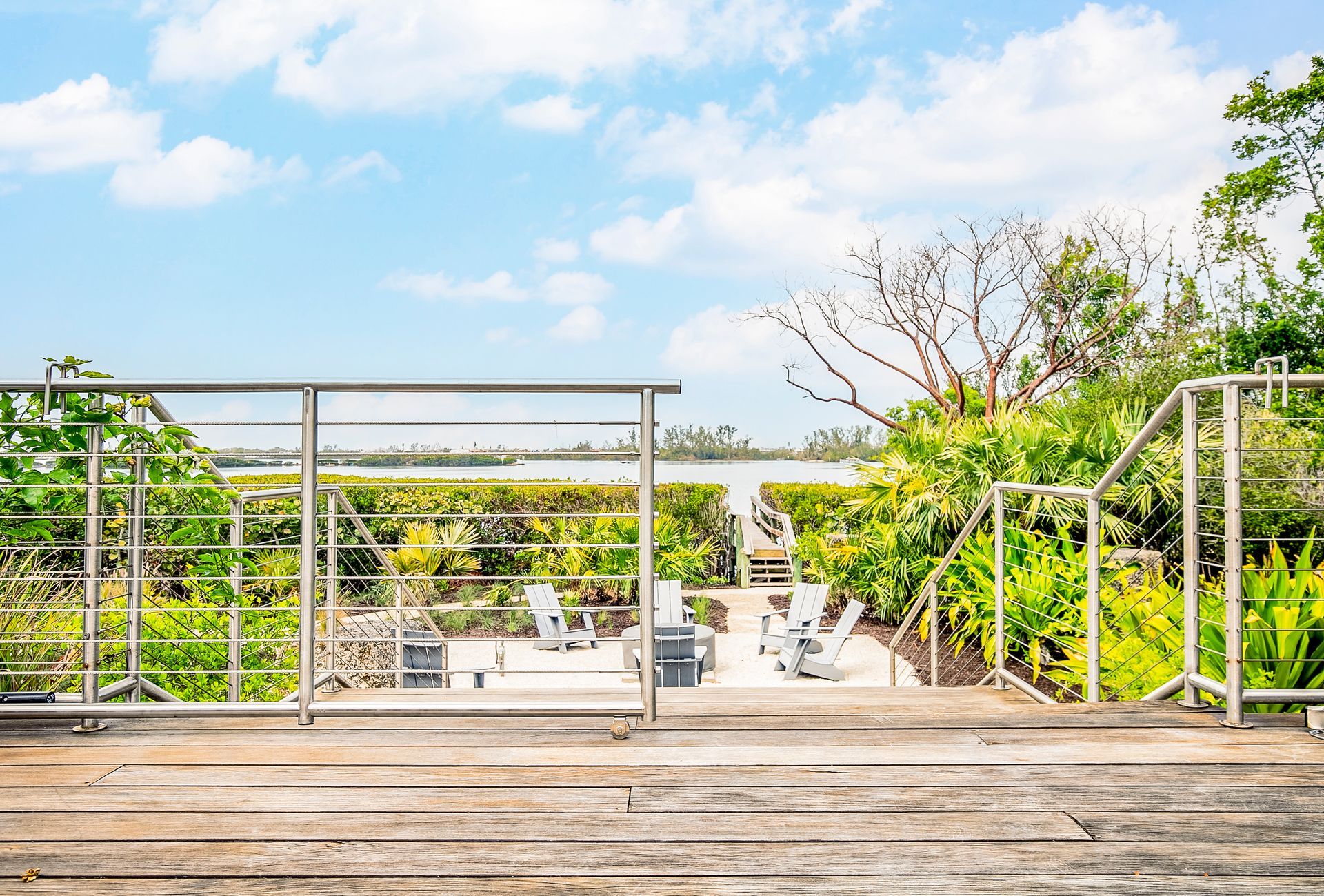 Wooden deck overlooking a lush garden and blue sky, with white railings and patio seating below
