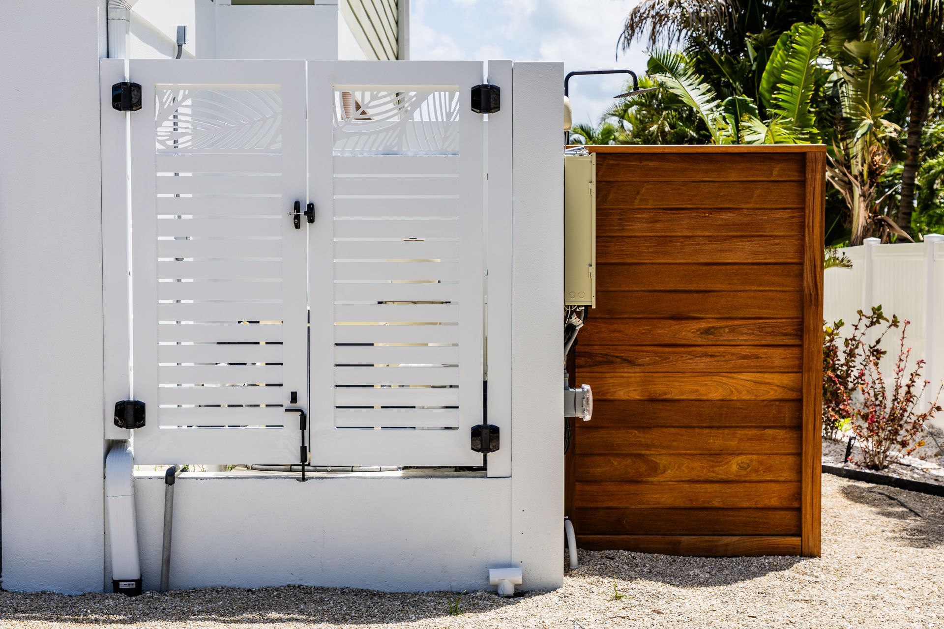 White metal gate beside a wooden fence and white wall in a sunny outdoor yard