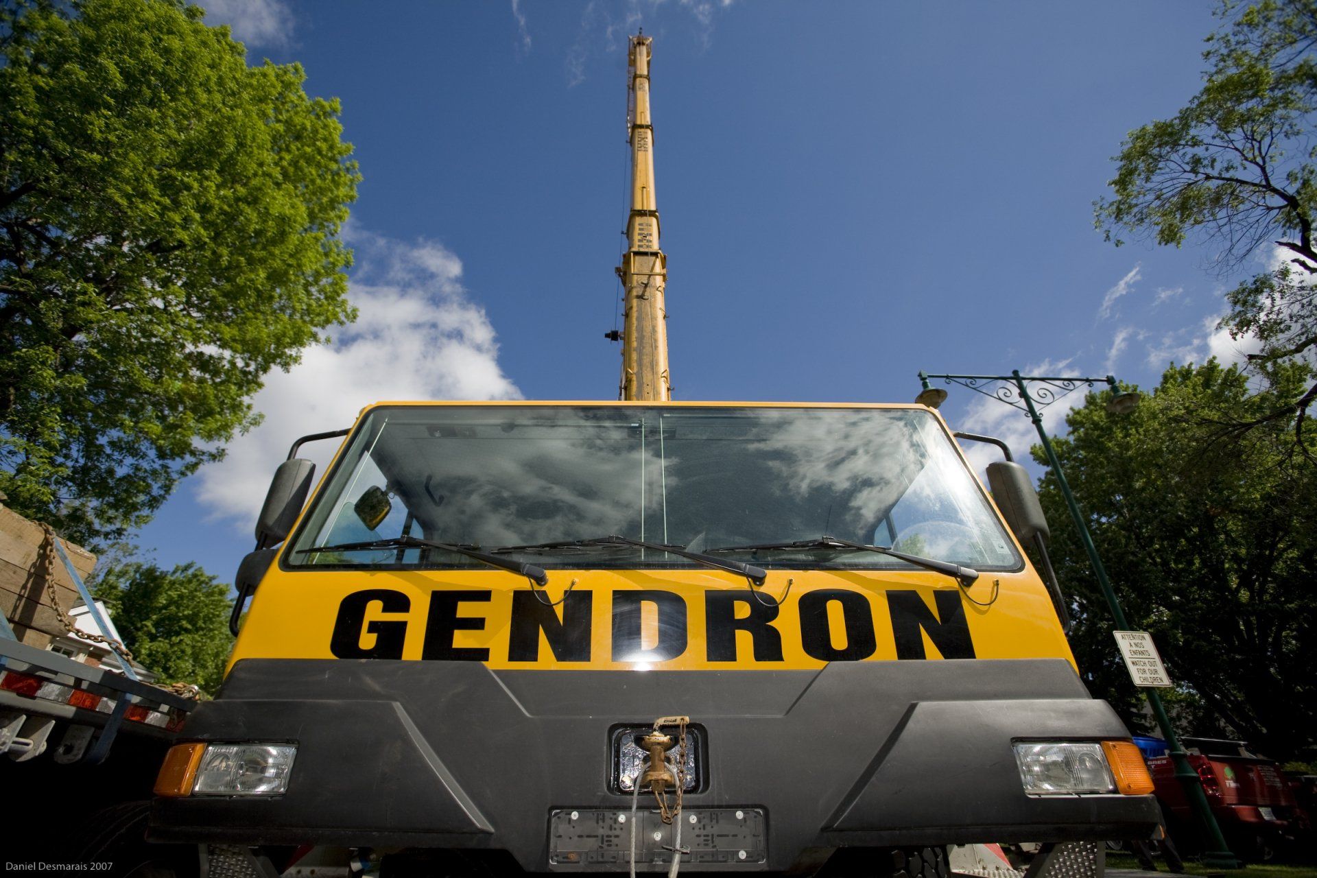 Camion-grue Gendron jaune sur fond de ciel bleu, flèche déployée, stationné en milieu urbain.