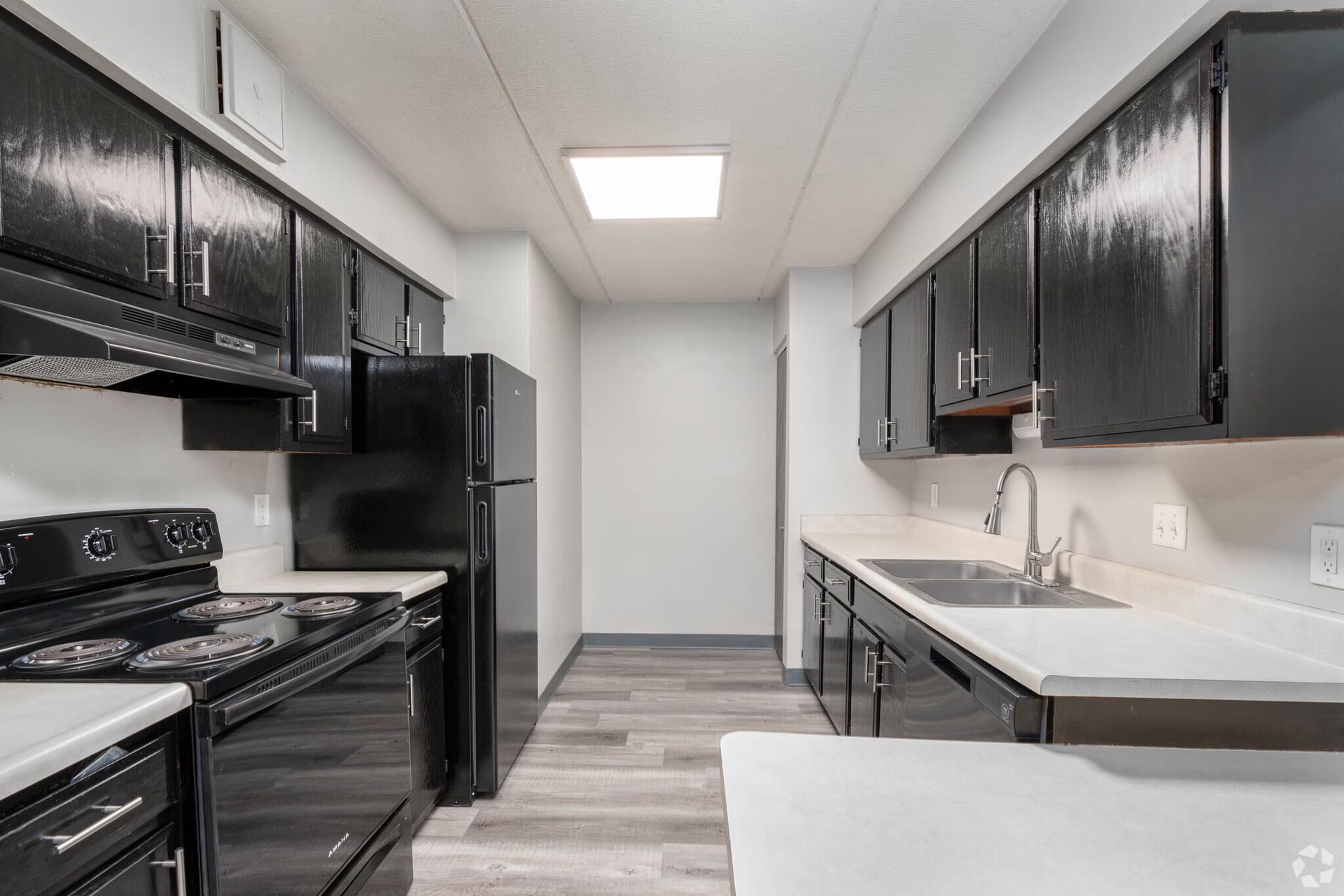 Black and white kitchen with stove, refrigerator, cabinets, and a sink on a wood-look floor.