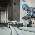 Worker in blue hard hat wiring cables in a construction site with exposed pipes and ducts