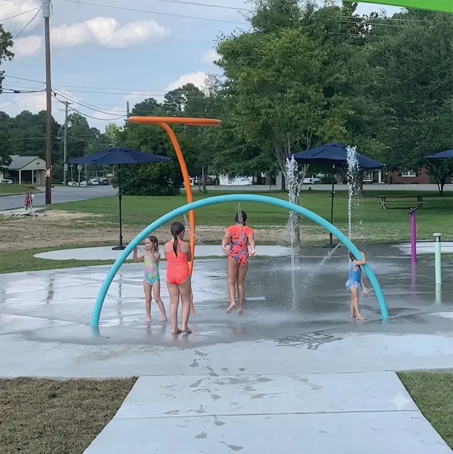 Children playing under a colorful splash pad arch in a park on a wet summer day