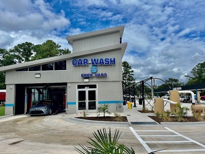 Modern car wash building with blue signage and a car entering the wash bay under a cloudy sky