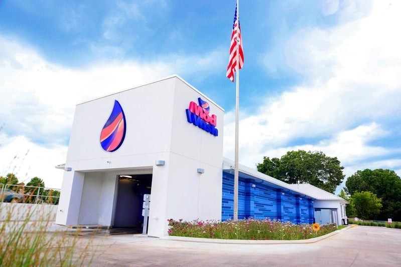 Exterior of a modern convenience store with a tall American flagpole and blue-tinted windows