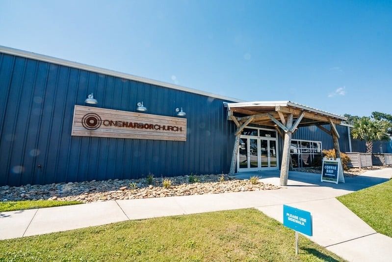 Blue building storefront with wood awning, sidewalk, and grassy lawn under a clear sky