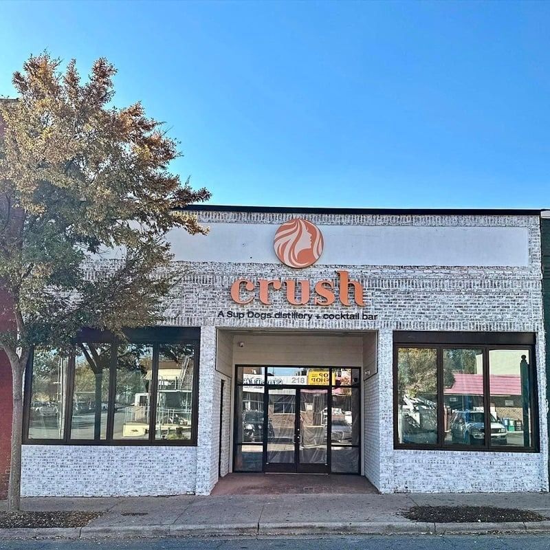 Storefront with a white brick facade and a “crush” sign above the entrance under a clear blue sky